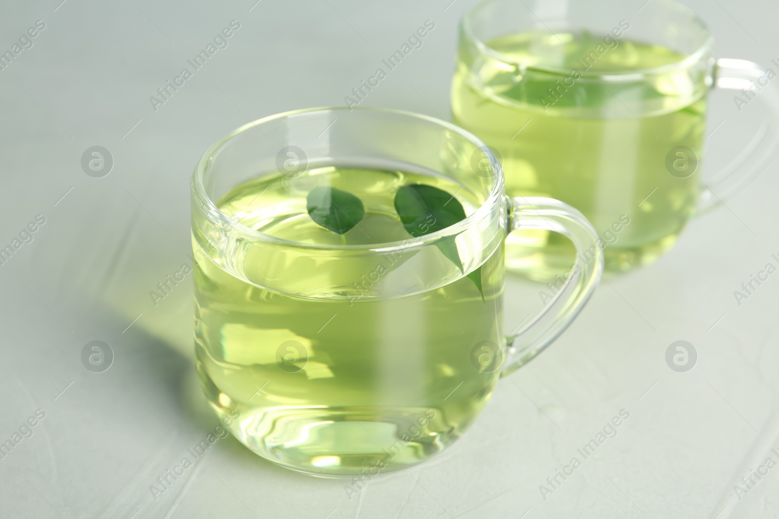 Photo of Cups of aromatic green tea on light table