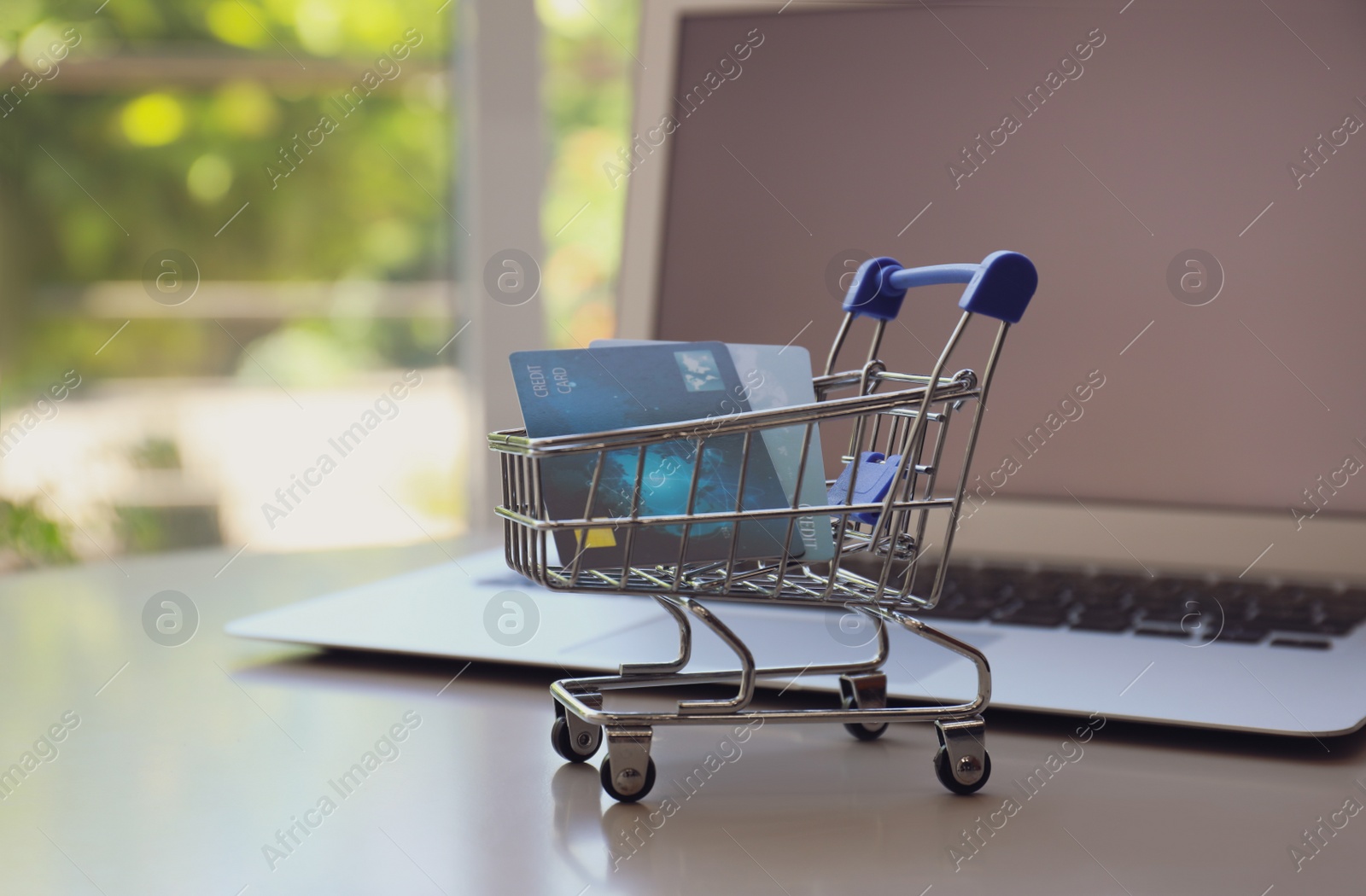 Photo of Internet shopping. Small cart with credit cards and laptop on table indoors
