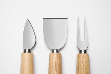 Cheese knives and fork on white background, top view
