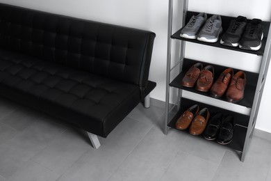 Photo of Shoe storage unit and stylish leather sofa near white wall in hallway. Interior design
