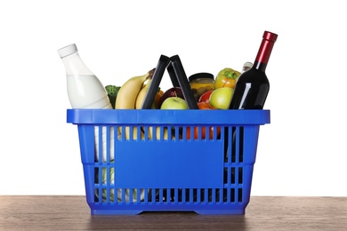 Photo of Shopping basket with grocery products on wooden table against white background