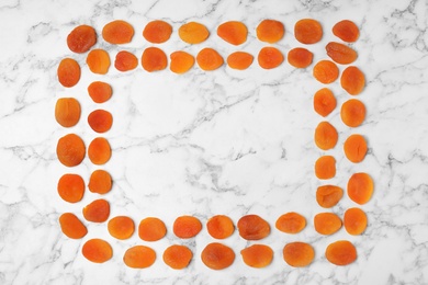 Photo of Frame made of apricots on marble background, top view with space for text. Dried fruit as healthy food
