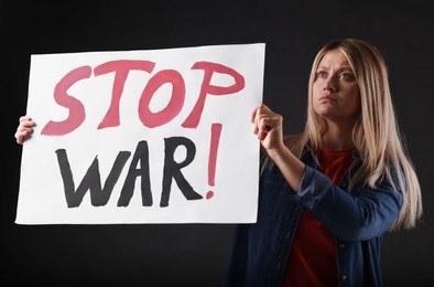 Photo of Sad woman holding poster with words Stop War on black background