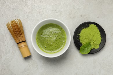 Photo of Cup of fresh matcha tea, green powder and bamboo whisk on light grey table, flat lay