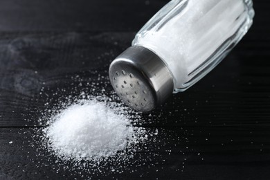 Organic salt in glass shaker on black wooden table, closeup