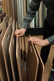 Photo of Man choosing wooden flooring among different samples in shop, closeup