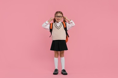 Photo of Happy schoolgirl in glasses with backpack on pink background