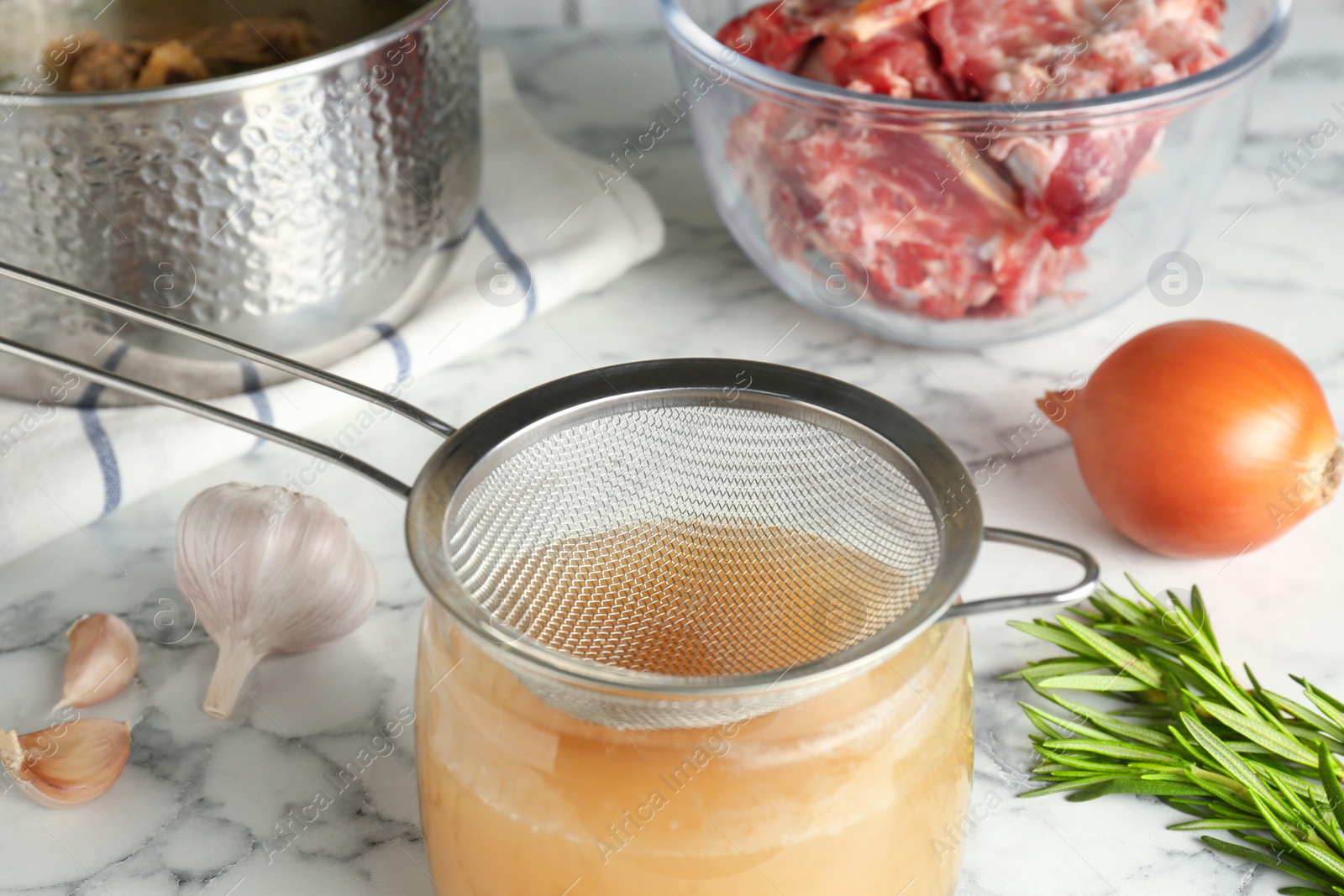 Photo of Straining delicious broth through sieve on white marble table, closeup