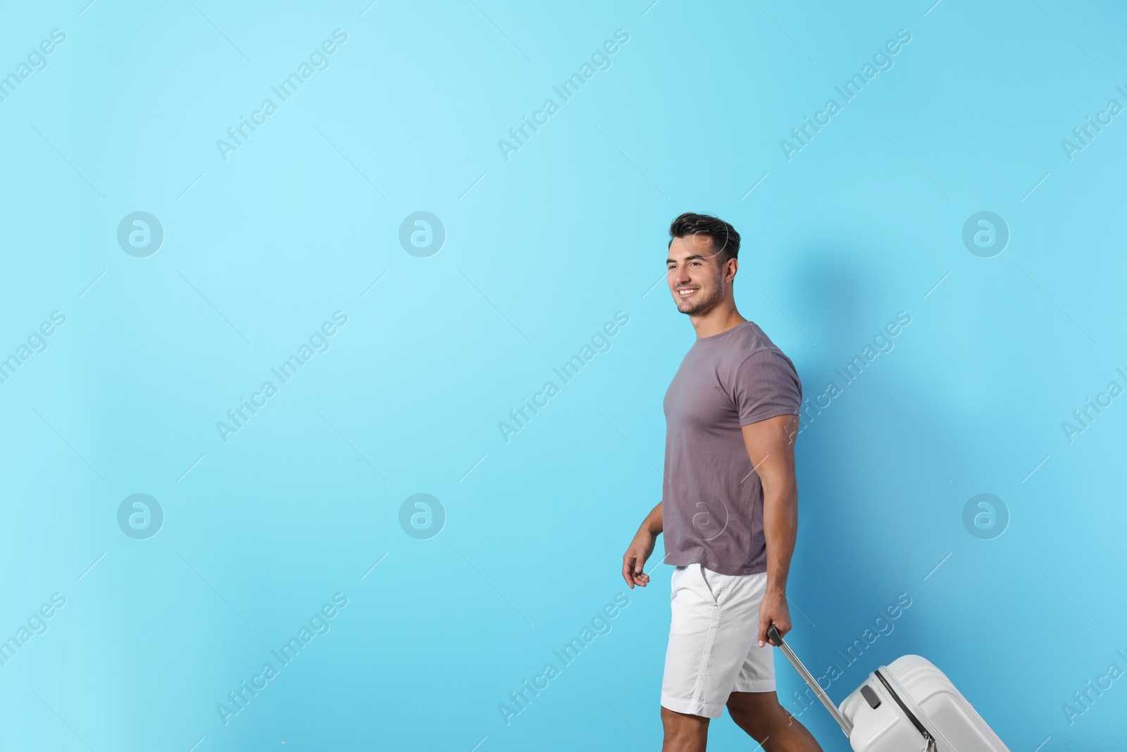 Photo of Young man walking with suitcase on color background