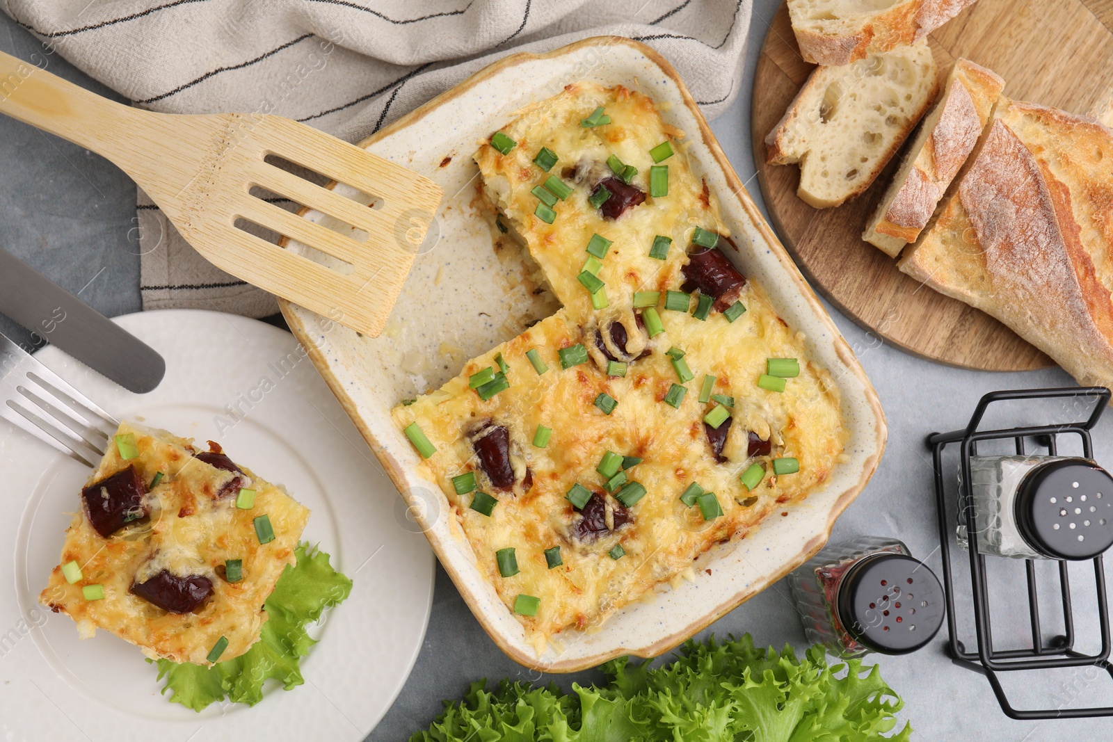 Photo of Tasty sausage casserole with green onions served on grey table, flat lay