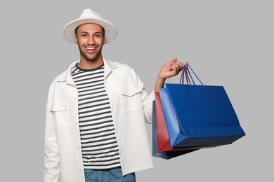 Happy African American man in hat with shopping bags on light grey background