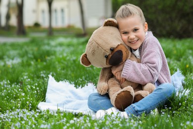 Little girl with teddy bear on plaid outdoors. Space for text