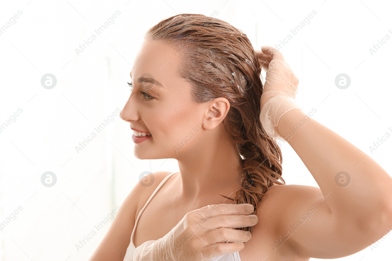 Photo of Young woman dyeing her hair against light background