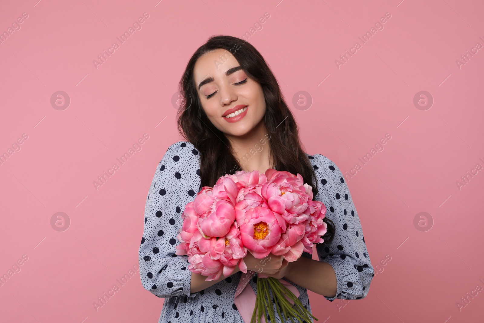 Photo of Beautiful young woman with bouquet of peonies on pink background