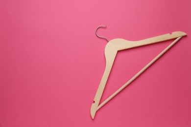 Empty wooden hanger on pink background, top view. Space for text