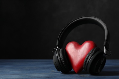 Photo of Decorative heart with headphones on table against dark background. Space for text