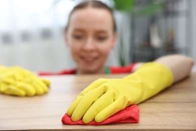 Photo of Woman cleaning wooden table with rag at home, selective focus