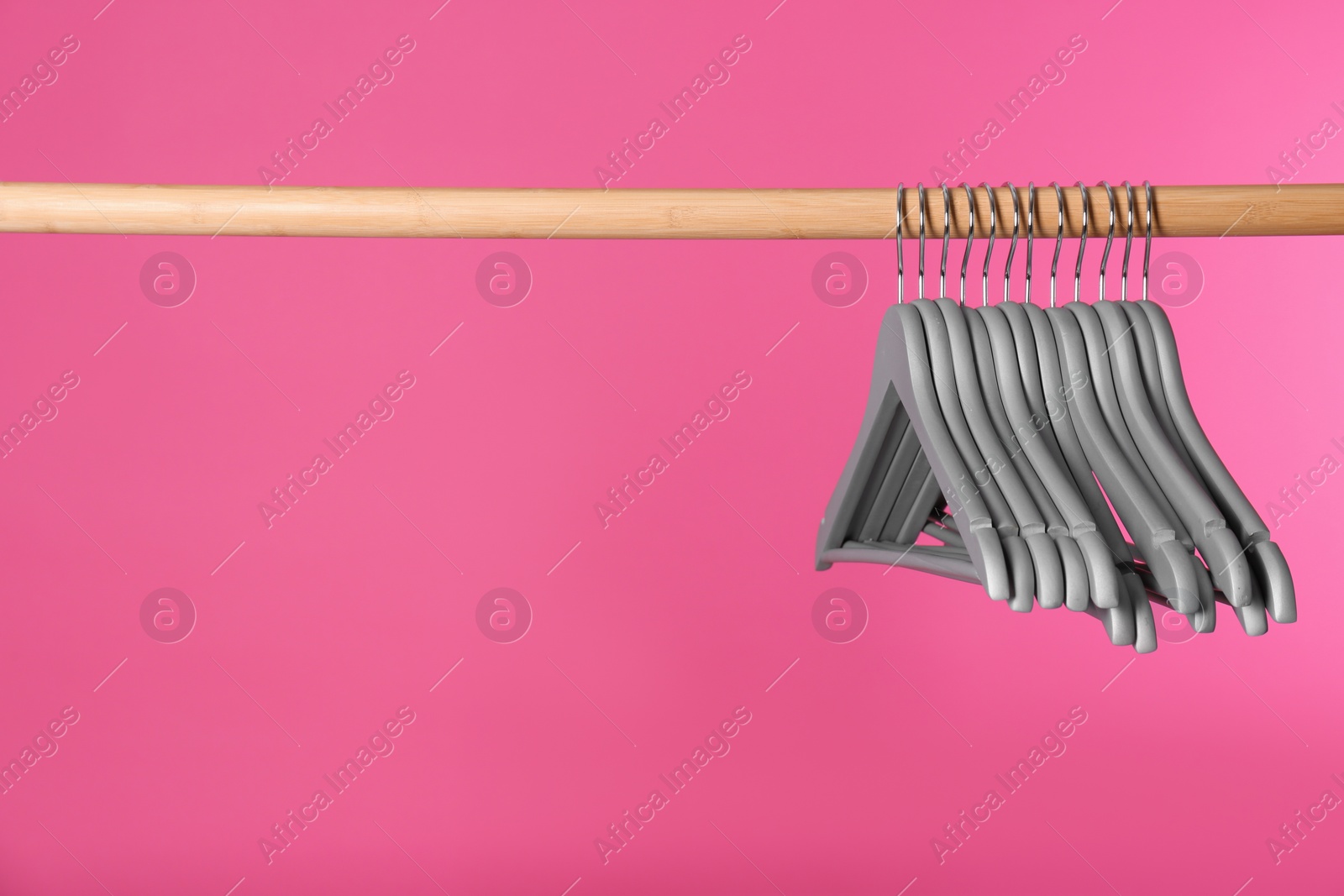 Photo of Wooden rack with clothes hangers on color background, space for text