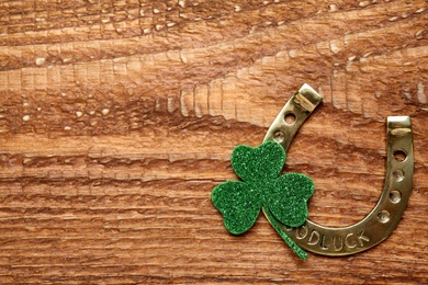 Photo of Golden horseshoe and decorative clover leaf on wooden table, flat lay with space for text. Saint Patrick's Day celebration