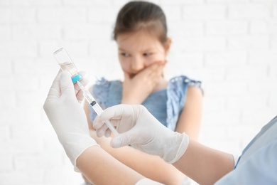 Doctor filling syringe with medicine and child on background. Vaccination day