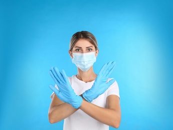 Photo of Woman in protective mask showing stop gesture on light blue background. Prevent spreading of COVID‑19