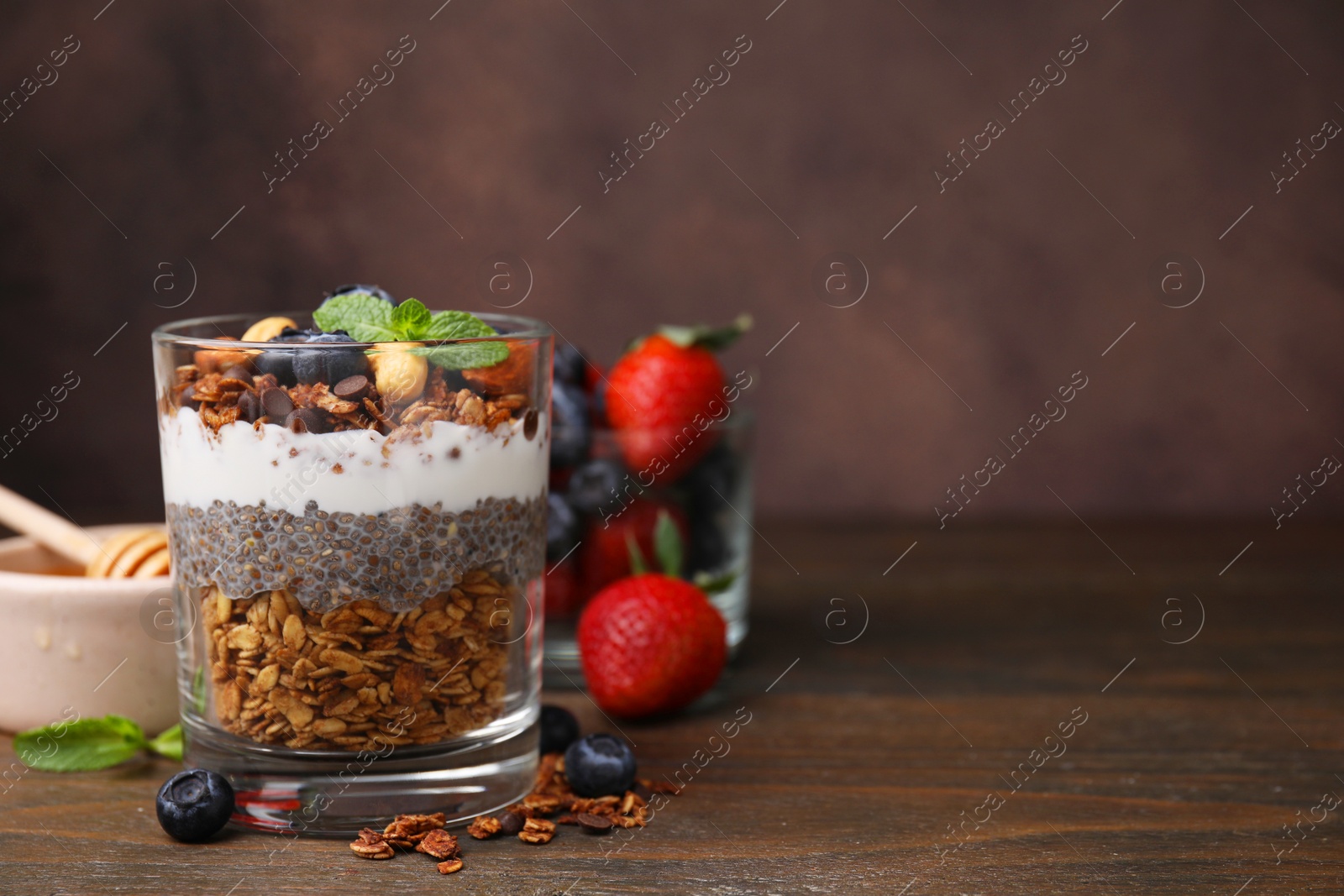 Photo of Tasty granola with berries, yogurt and chia seeds in glass on wooden table, space for text