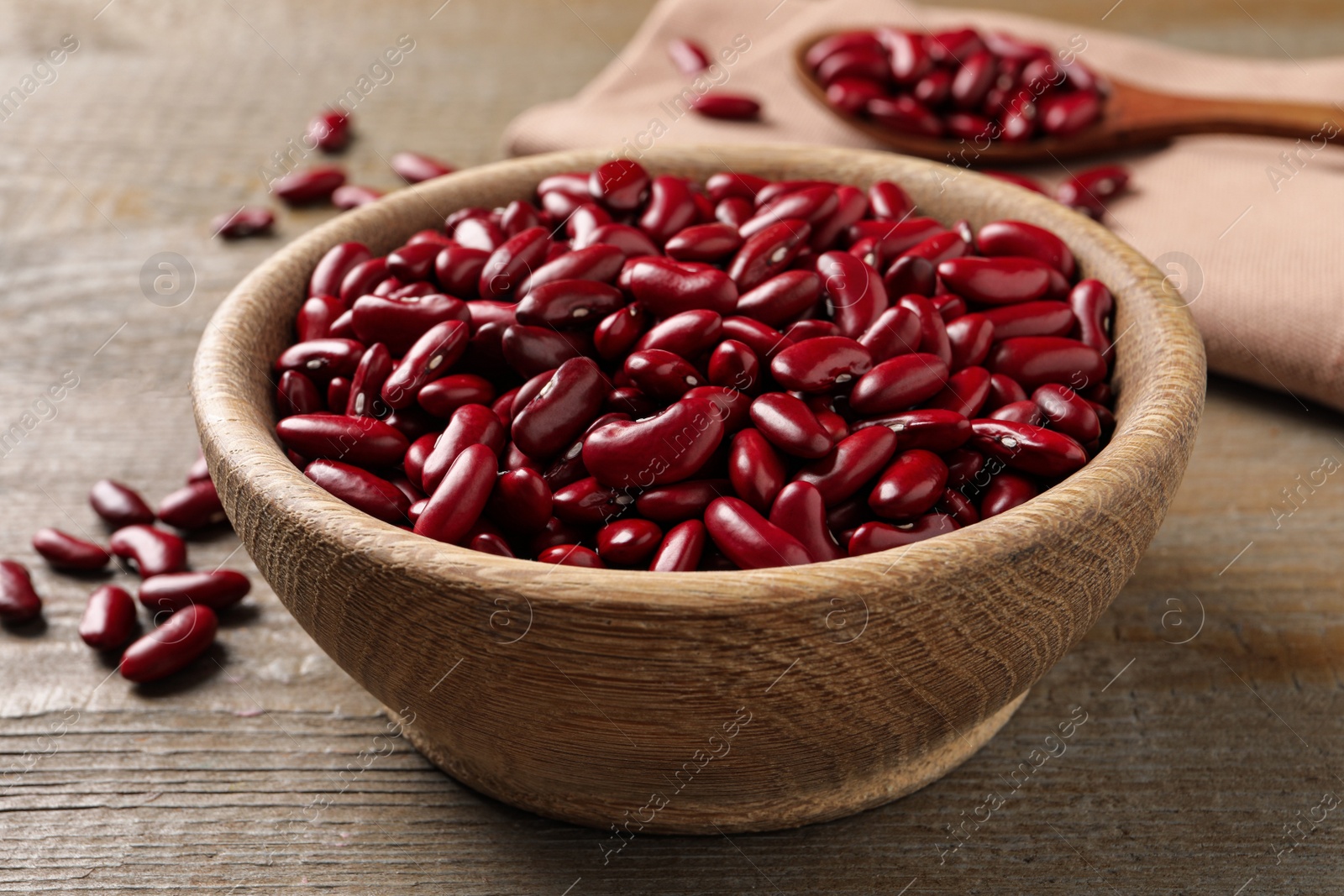 Photo of Raw red kidney beans in bowl on wooden table, closeup