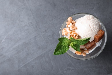 Glass bowl of ice cream with caramel candies, mint and popcorn on grey table, top view. Space for text