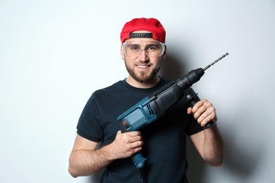 Photo of Young working man with rotary hammer on light background