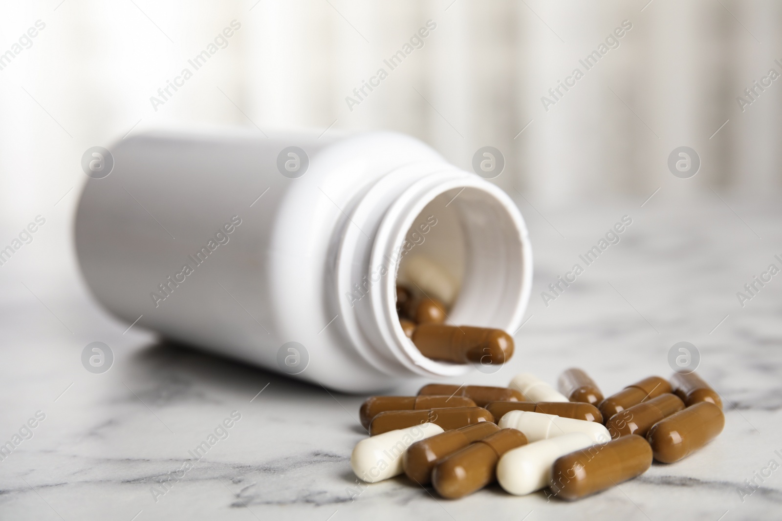 Photo of Bottle with vitamin pills on white marble table, closeup