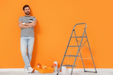 Photo of Designer and painting equipment near freshly painted orange wall indoors