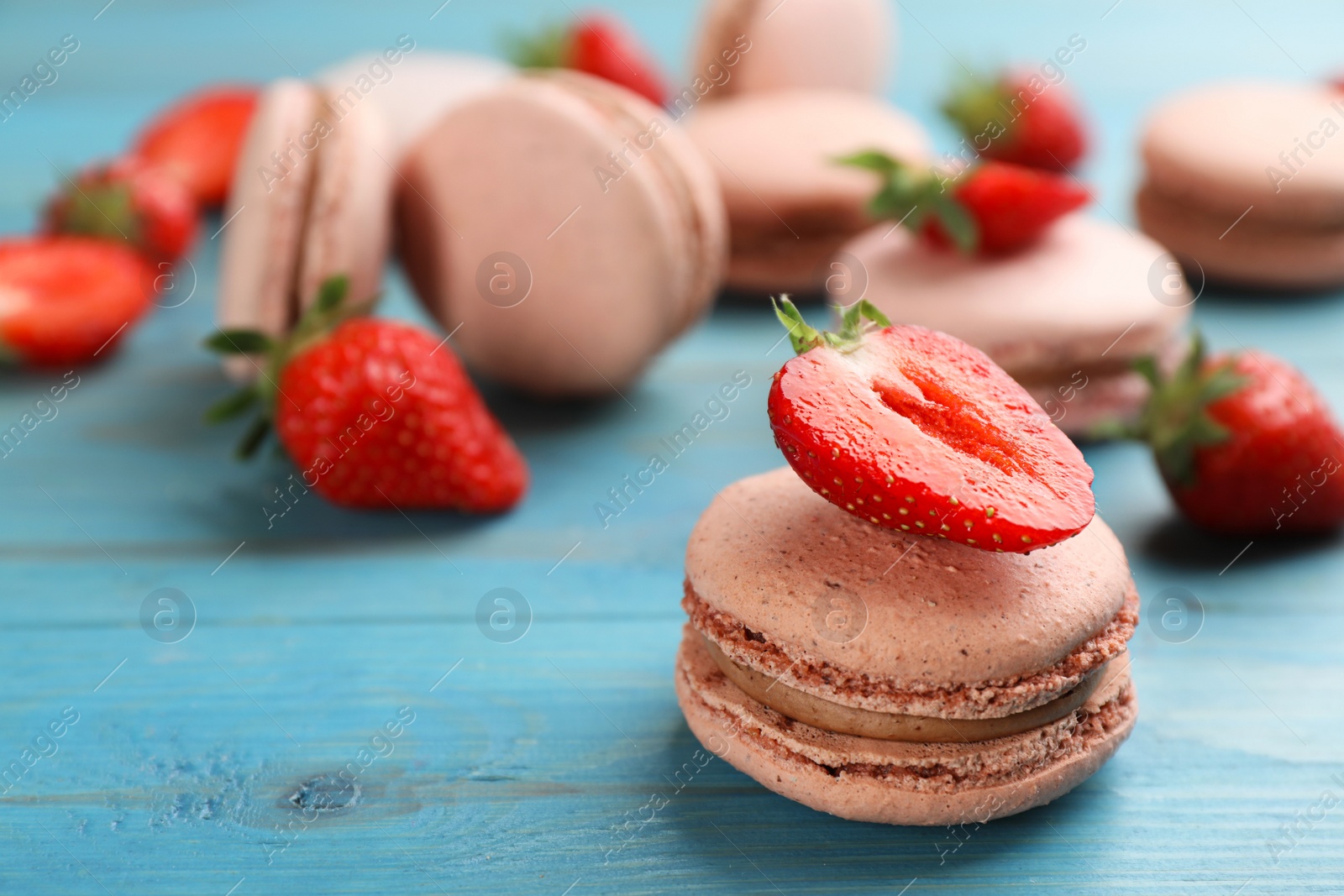 Photo of Delicious macarons and strawberries on light blue wooden table, closeup. Space for text