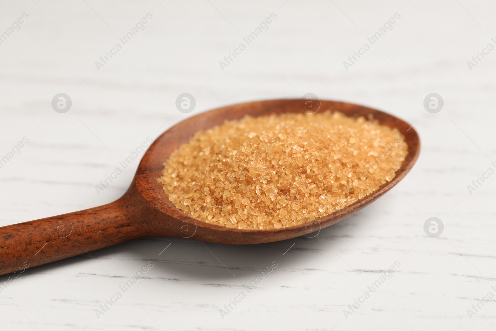 Photo of Spoon with brown sugar on white wooden table, closeup