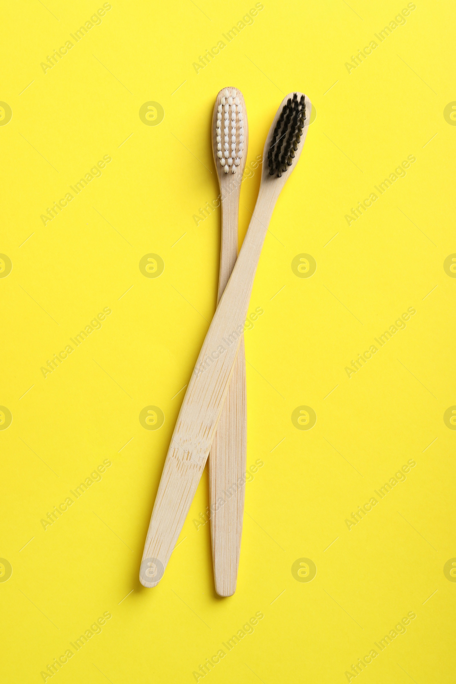 Photo of Two bamboo toothbrushes on yellow background, flat lay