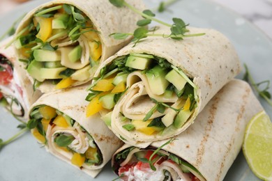 Photo of Delicious sandwich wraps with fresh vegetables and slice of lime on table, closeup
