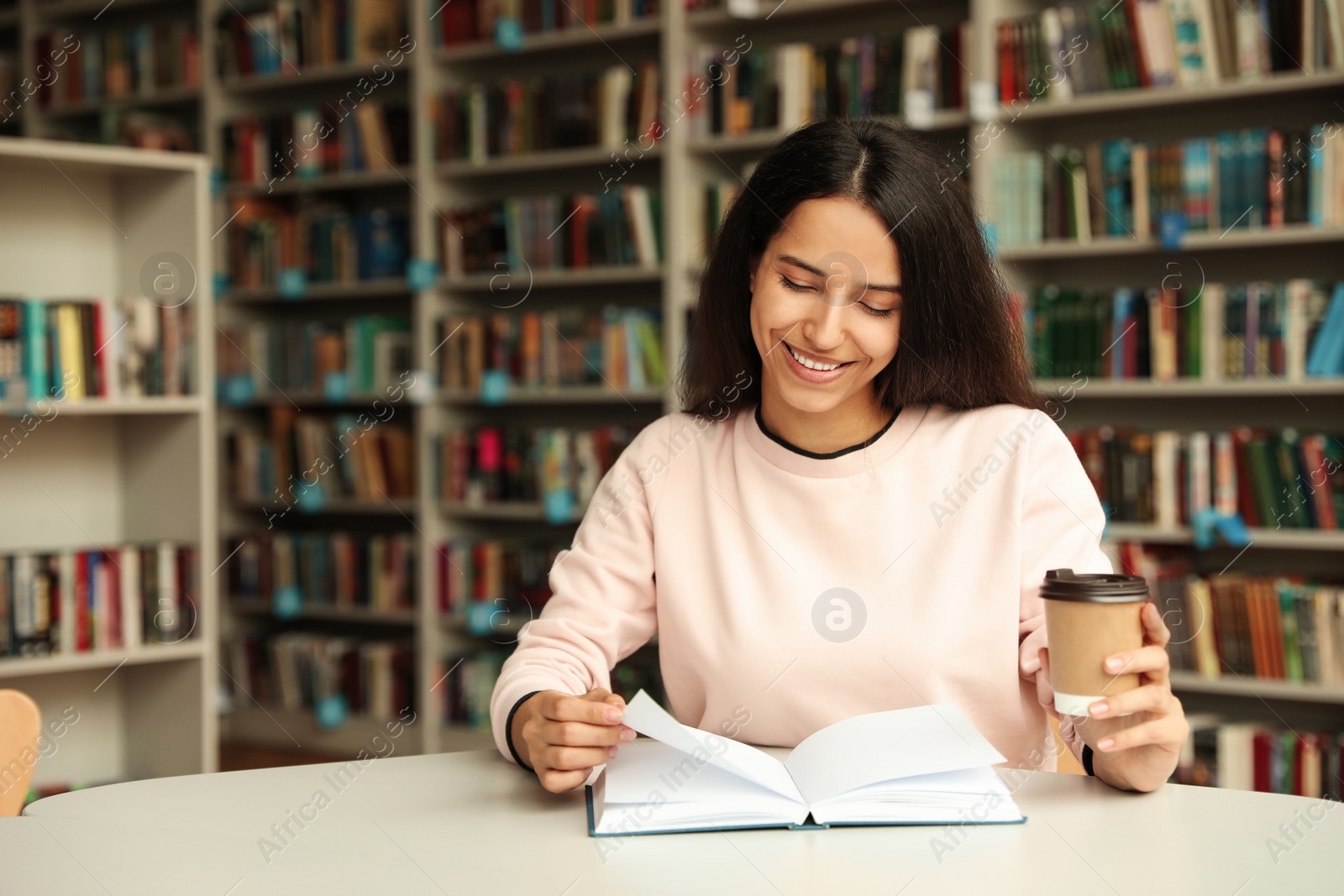 Photo of Young woman reading book at table in library. Space for text