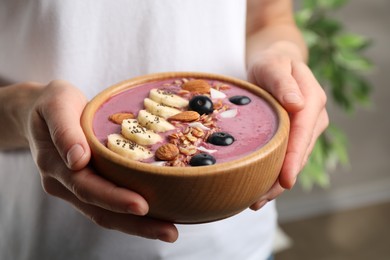 Photo of Woman holding dessert bowl with delicious acai smoothie, closeup view