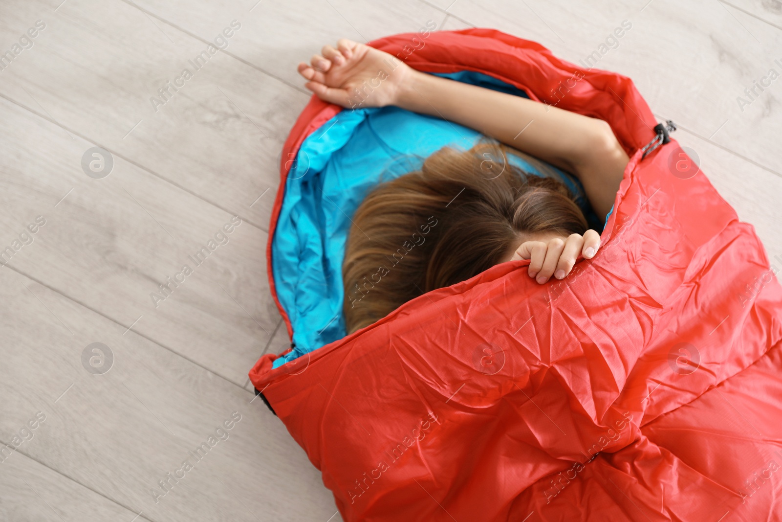 Photo of Young woman in comfortable sleeping bag on floor, top view. Space for text