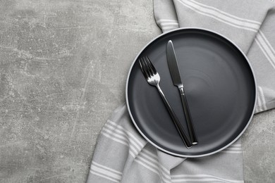 Photo of New dark plate with cutlery and napkin on light grey table, top view. Space for text