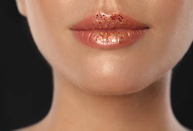 Young woman with glitter makeup on black background, closeup view