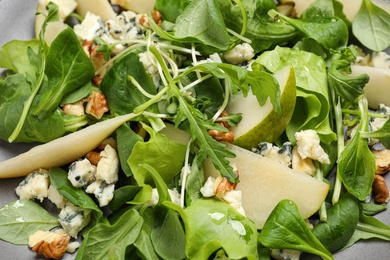 Tasty salad with pear slices, arugula and walnuts as background, closeup