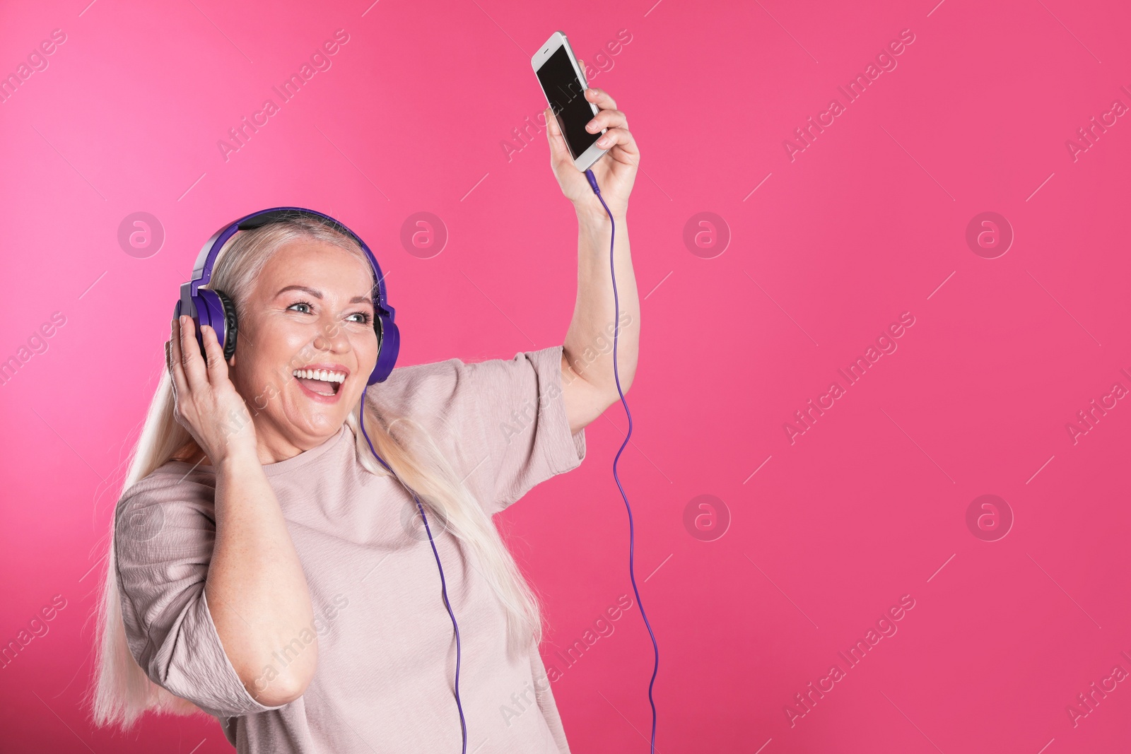 Photo of Mature woman in headphones with mobile device on color background. Space for text