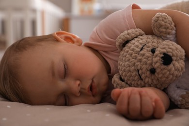 Photo of Adorable little baby with toy bear sleeping on bed at home, closeup