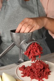 Woman making beef mince with manual meat grinder at light wooden table, closeup
