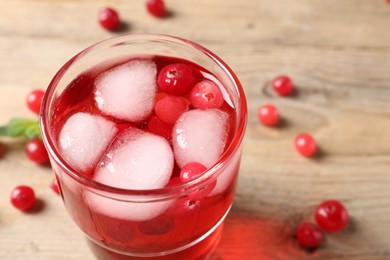 Tasty cranberry juice with ice cubes in glass and fresh berries on wooden table, closeup