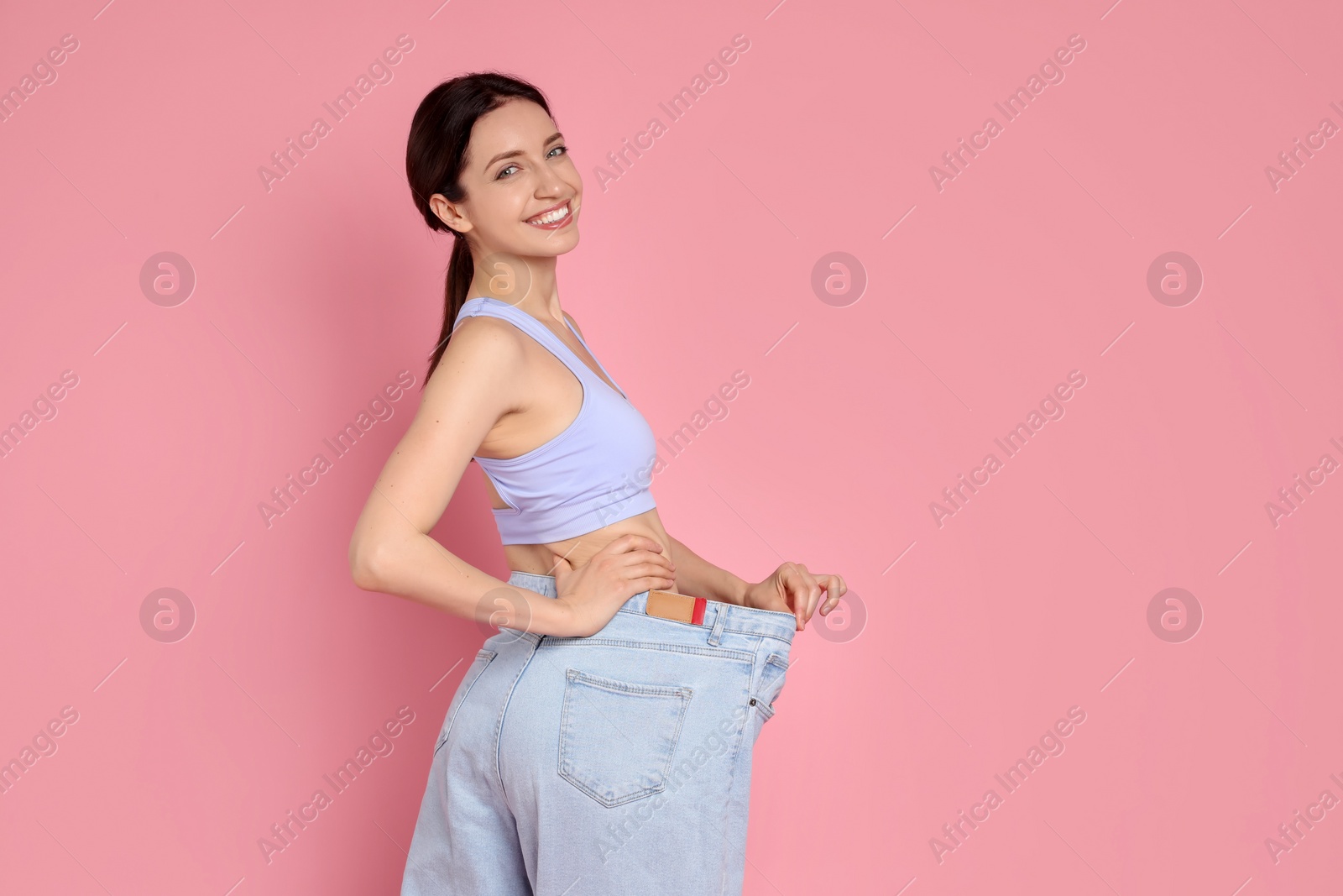 Photo of Happy young woman in big jeans showing her slim body on pink background, space for text