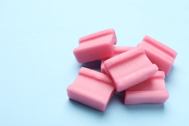 Photo of Tasty pink chewing gums on light blue background, closeup. Space for text