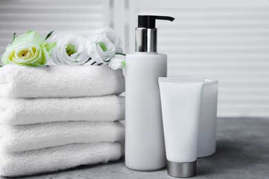 Towels, cosmetic products and flowers on grey table indoors