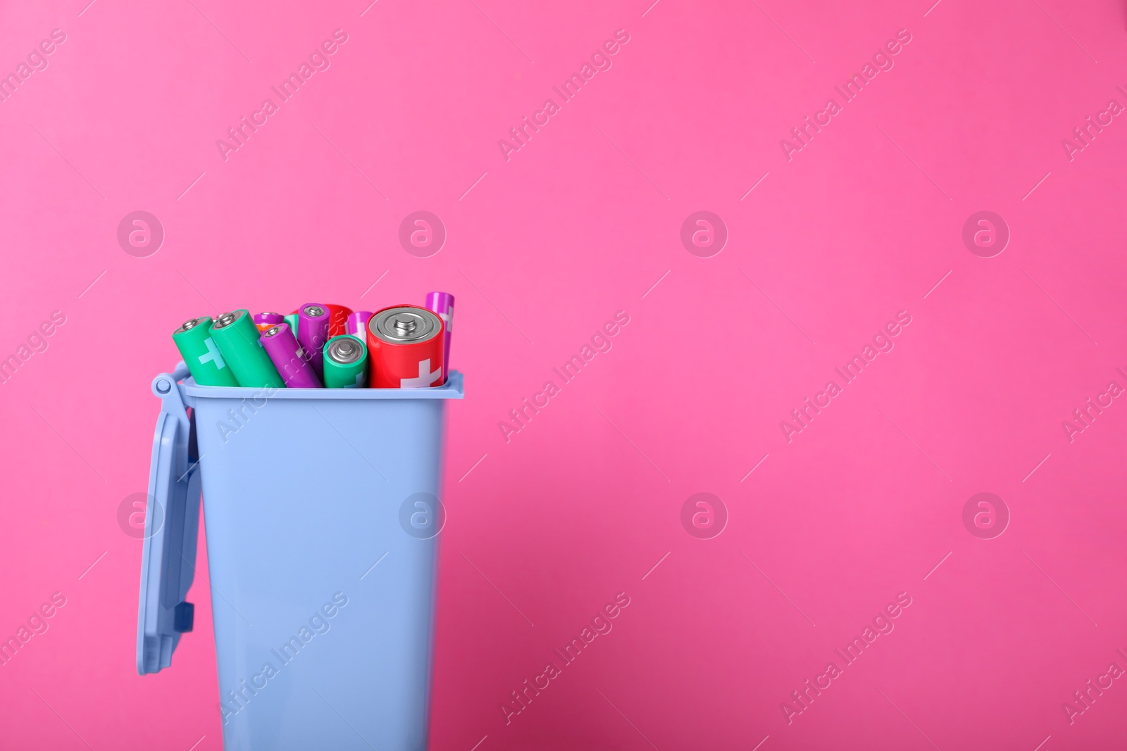 Photo of Many used batteries in recycling bin on pink background. Space for text