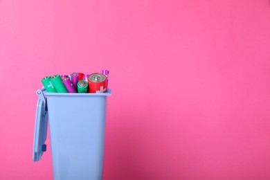 Many used batteries in recycling bin on pink background. Space for text
